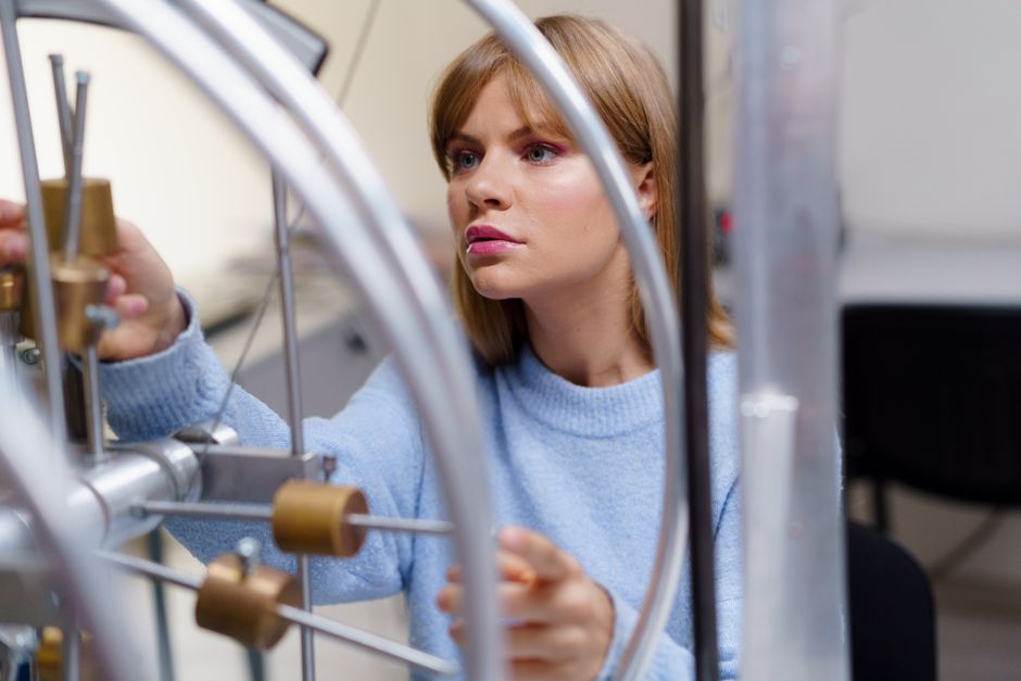 A woman in a blue sweater conducts a physics experiment in a science lab. Focused and intriguing.
