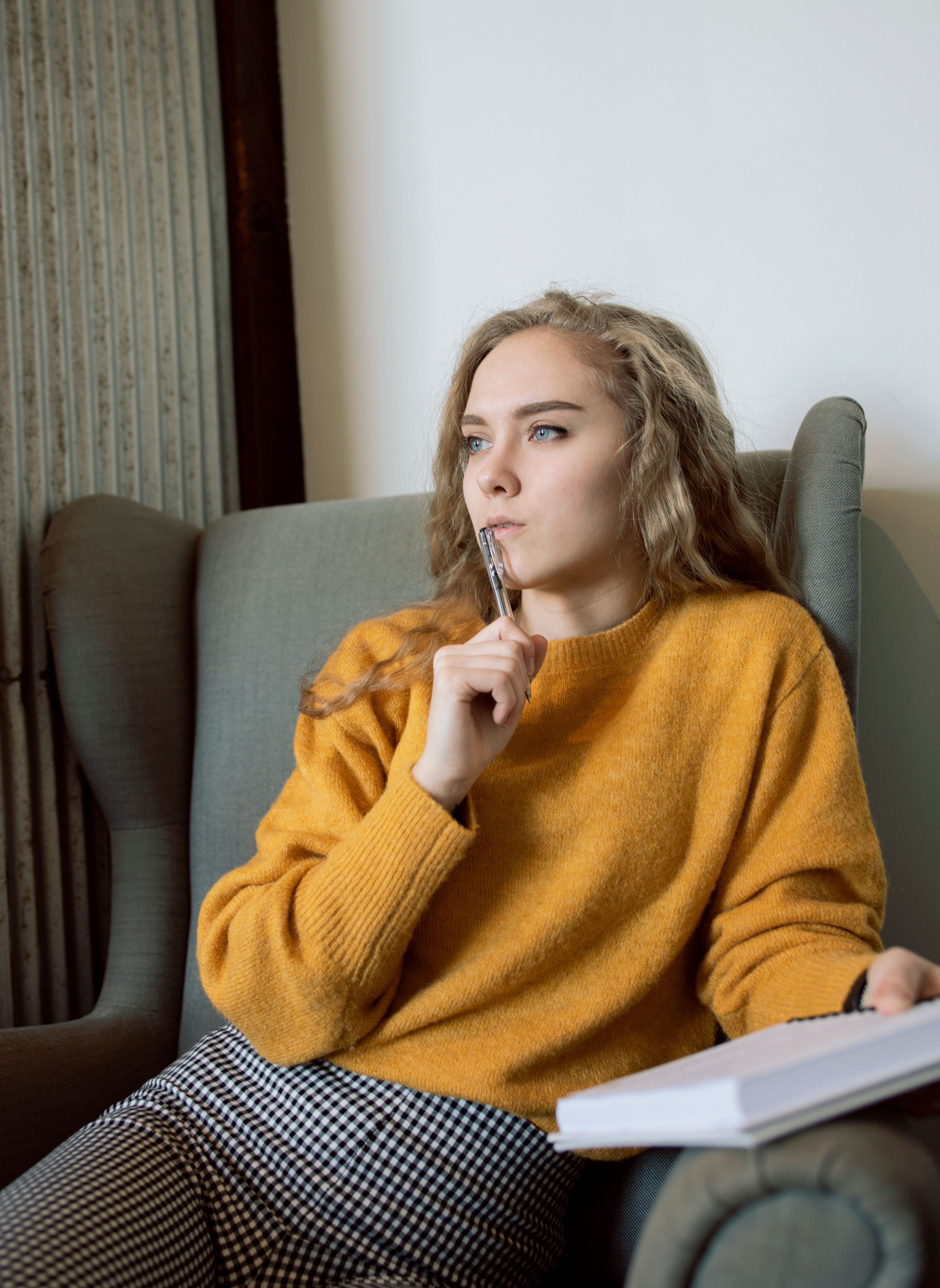 A woman in a mustard sweater sitting in an armchair with a notebook and pen
