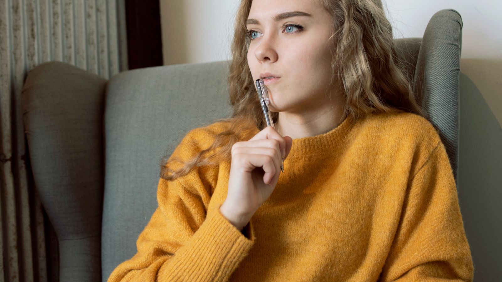 A woman in a mustard sweater sitting in an armchair with a notebook and pen