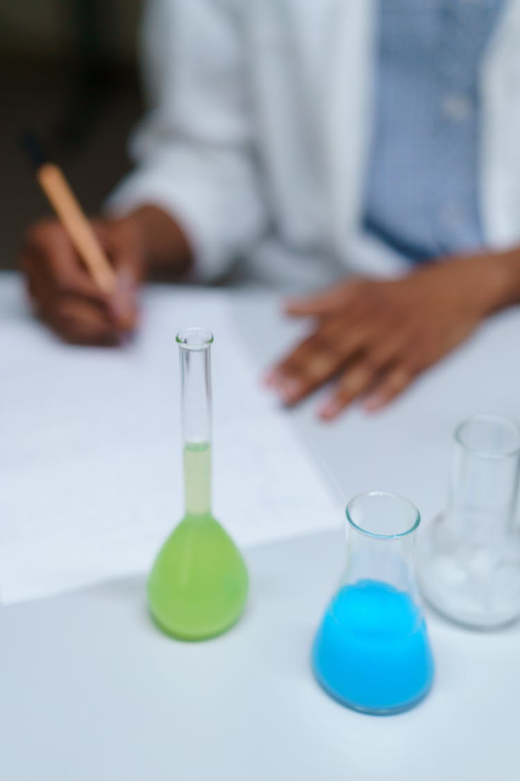 Person Writing On Table With Flasks  