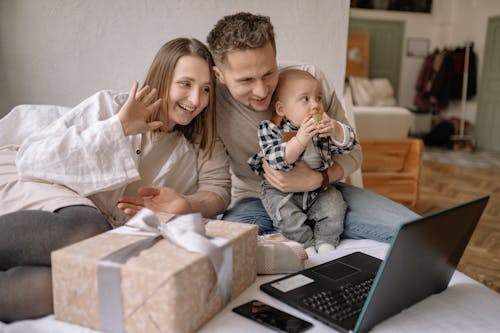 Free Couple Sitting on Bed with Their Son while Having a Video Call on Laptop Stock Photo