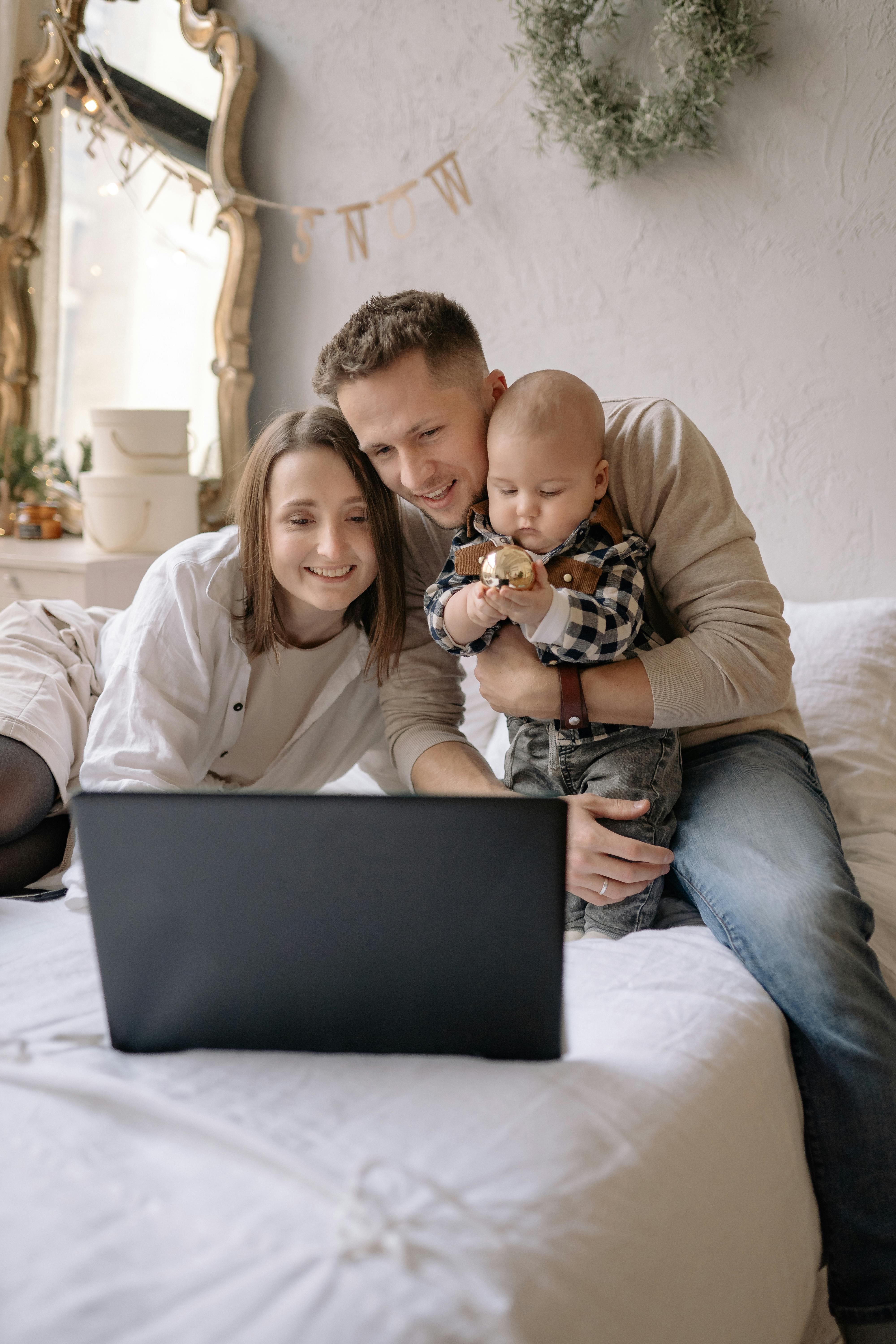 couple sitting on bed with their son while having a video call on laptop