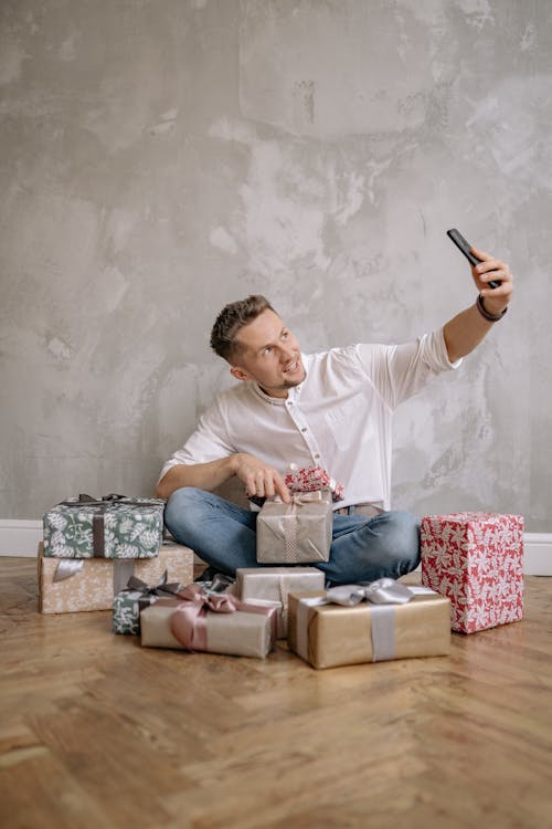 Free Man Sitting on the Floor Surrounded by Gifts Taking Selfie  Stock Photo
