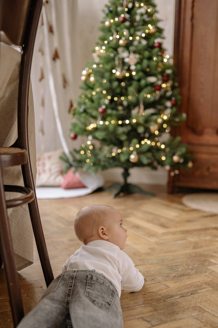 Baby In White Shirt Crawling On Floor Beside Christmas Tree