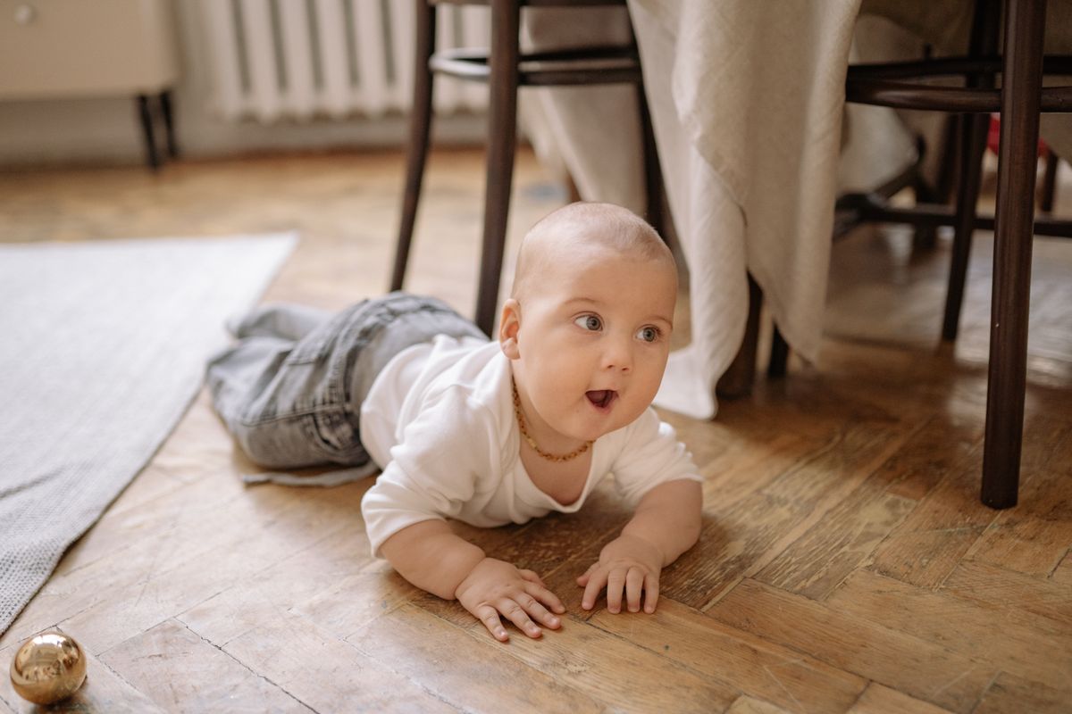 Baby crawling on a wooden floor exploring under furniture at home