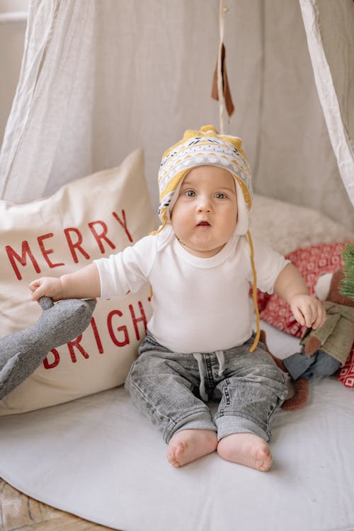 Free An Adorable Baby Boy With Headwear Sitting Beside Throw Pillows Stock Photo