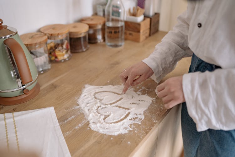 Person Standing In A Kitchen And Drawing Heart Shapes In Flour