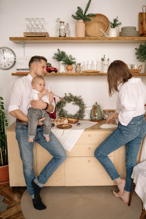 Free Family bonding in a cozy kitchen with Christmas decor, father holding baby while mother cooks. Stock Photo