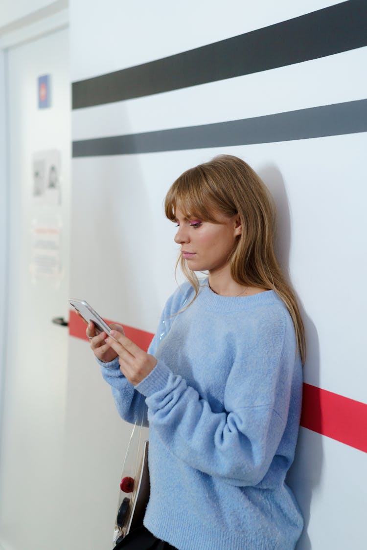 Young Woman Standing In A School Hallway And Looking At Her Phone 