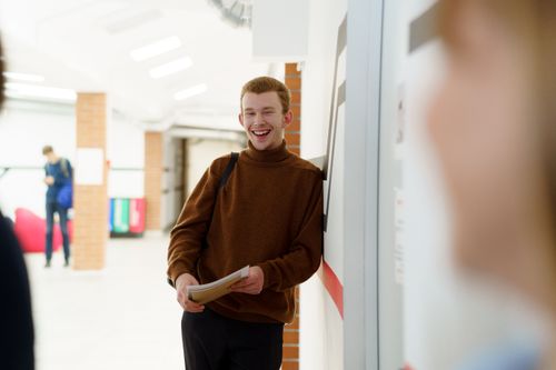 Free Happy teenage student smiling in a school hallway, holding a notebook. Perfect for education and back-to-school themes. Stock Photo