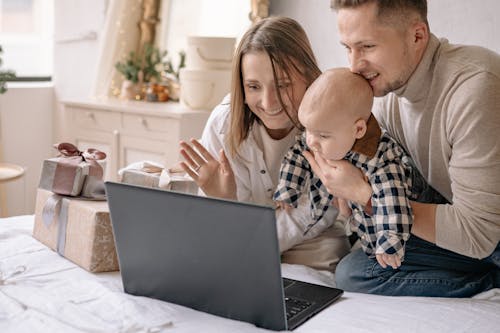Close-Up Shot of Couple Sitting on Bed with Their Son while Looking at a Laptop