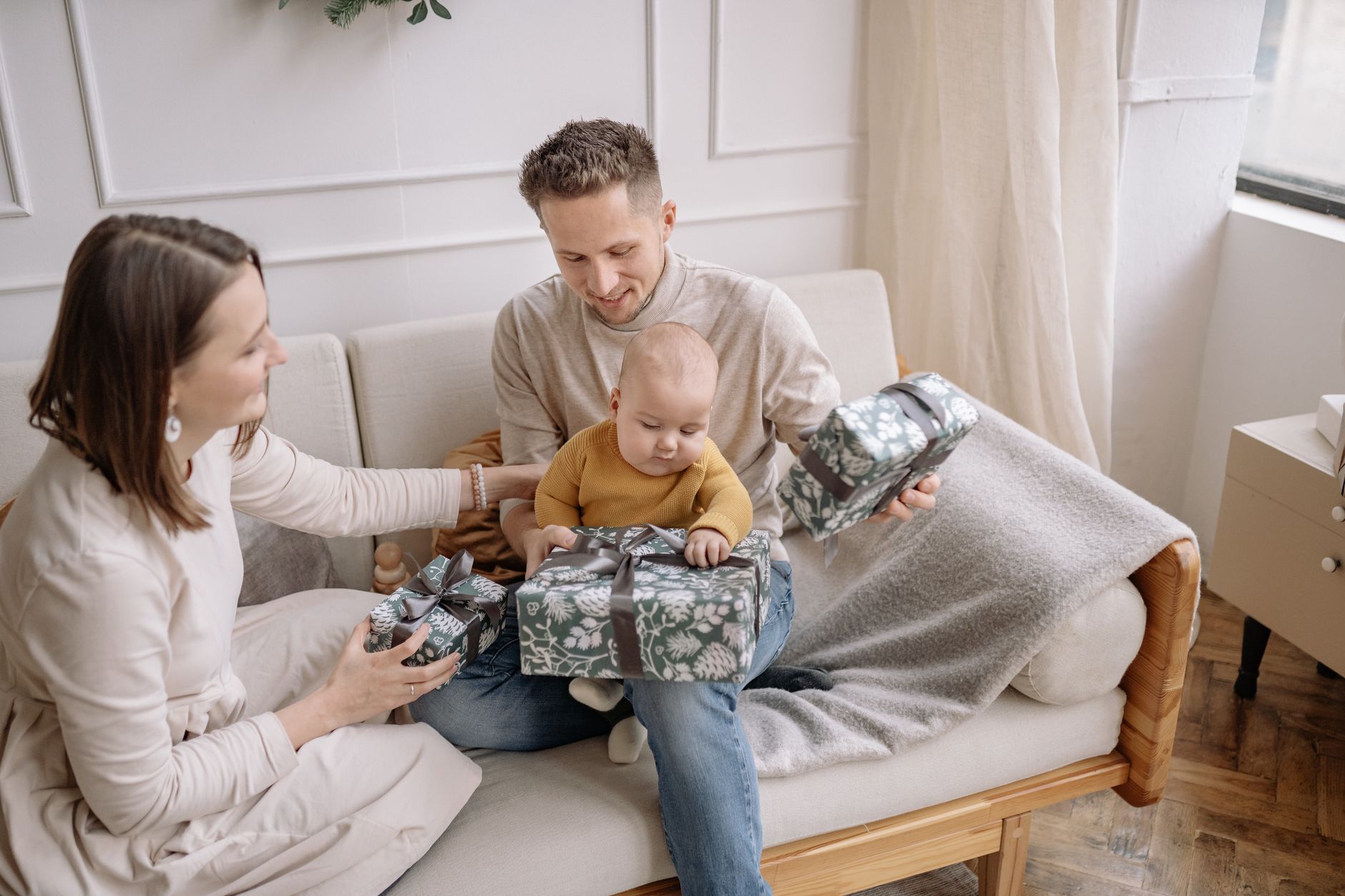 A happy family with a baby opening Christmas presents together on the couch indoors.