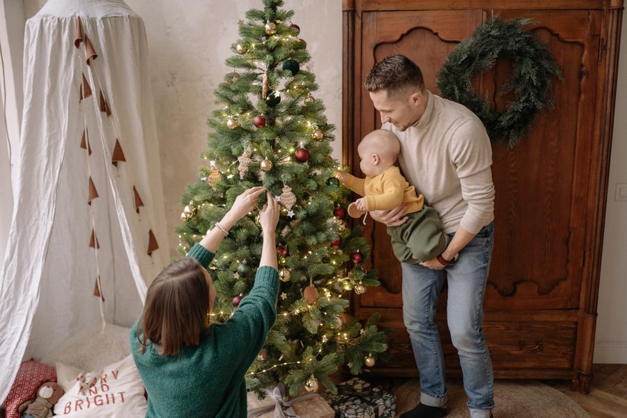 family decorating a Christmas tree together with a baby for a first Christmas keepsake photo