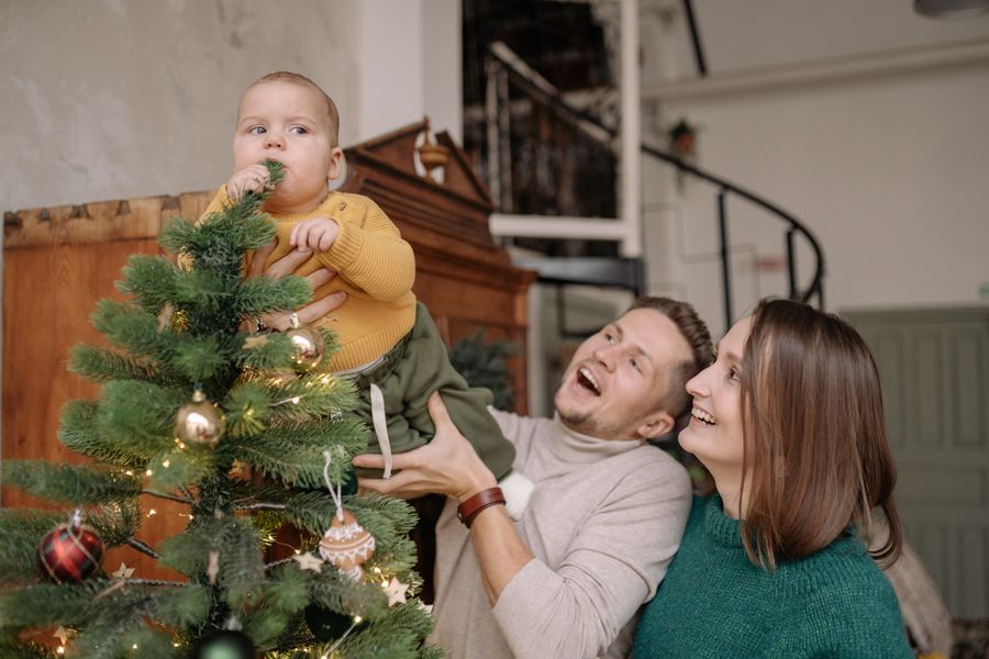 parents holding a baby beside a decorated Christmas tree while making holiday keepsake memories