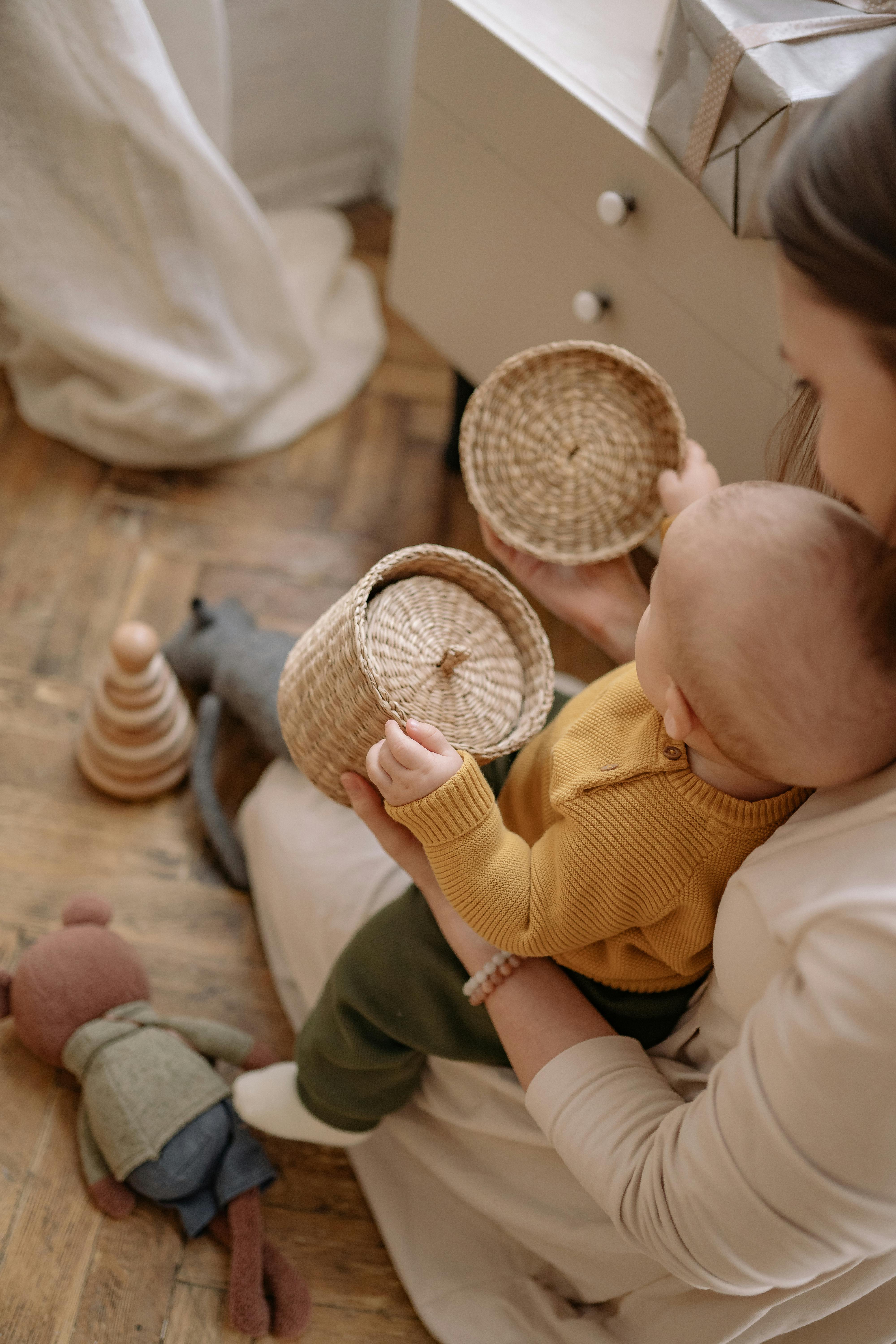 high angle view of woman sitting on floor with a baby and playing with baskets