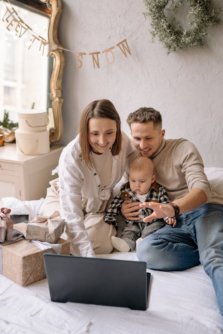 A Couple Looking At The Laptop Screen With Their Baby