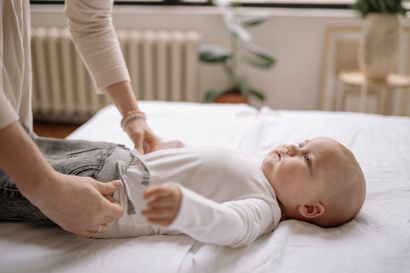 A mother lovingly dresses her baby on a bed, showcasing a tender parenting moment indoors.