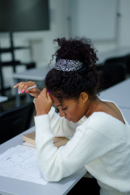 Free A young woman deeply concentrating while sitting at a desk with study materials. Stock Photo
