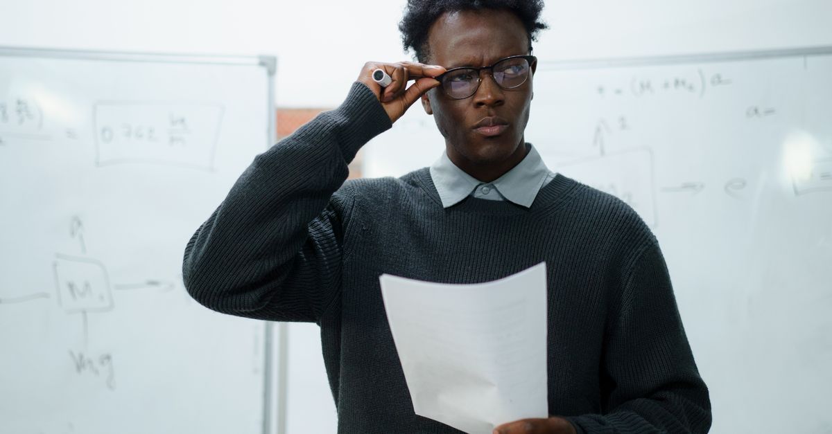 Person looking thoughtfully at a piece of paper in front of a whiteboard of notes