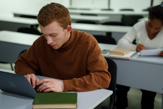 Two students focusing on work in a classroom setting, using laptops.