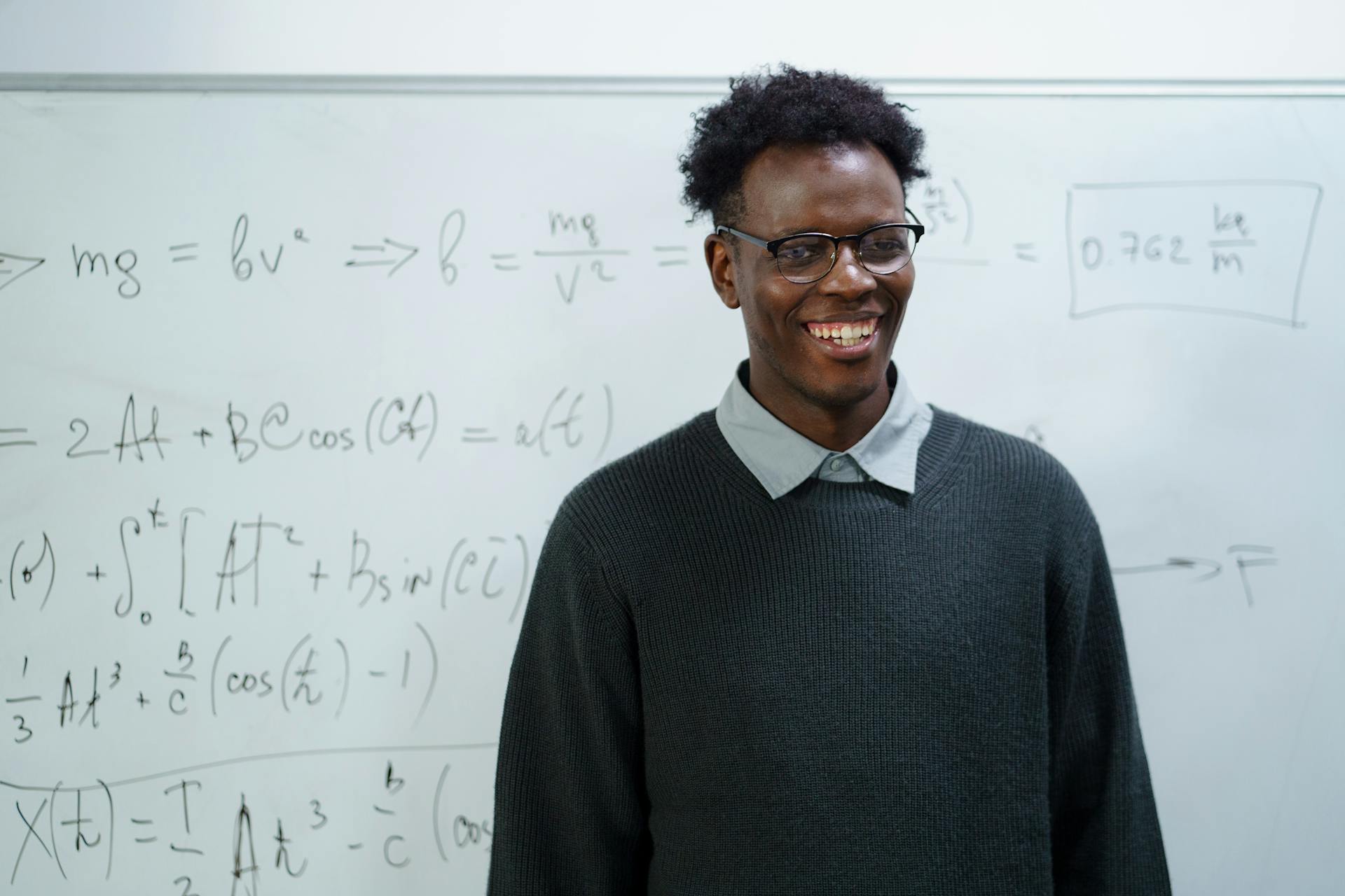 A cheerful professor with glasses teaching math in a classroom with a whiteboard.