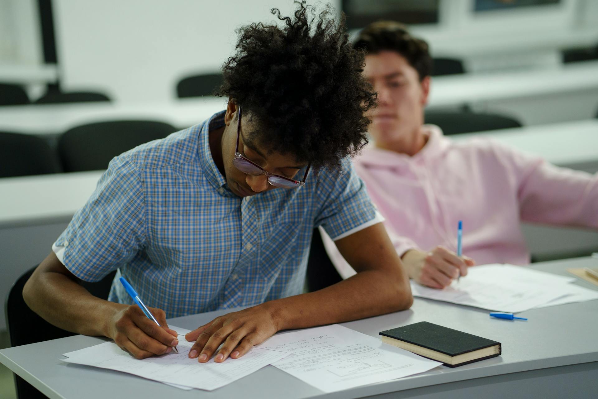 Two students focused on studying and writing notes in a classroom.