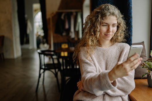 A young woman in a cozy sweater using her smartphone at home, enjoying a relaxed moment.