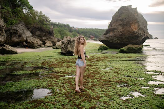 A woman explores a scenic beach with seaweed and rocks at sunset, embodying summer vibes.