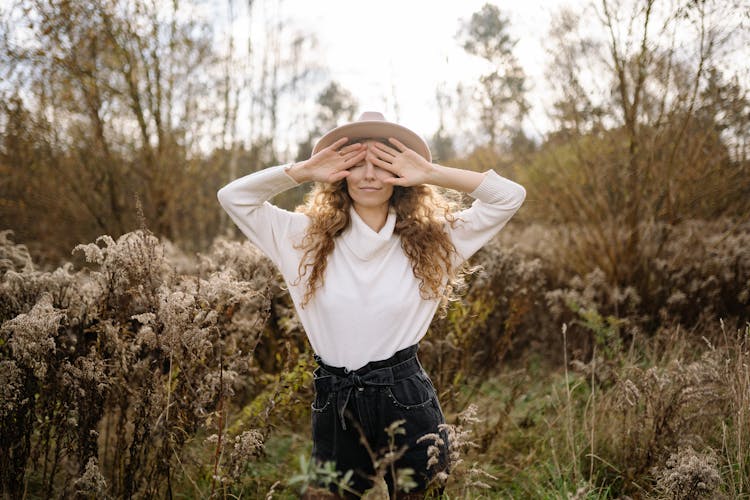 Woman Standing In Field Covering Face With Hands