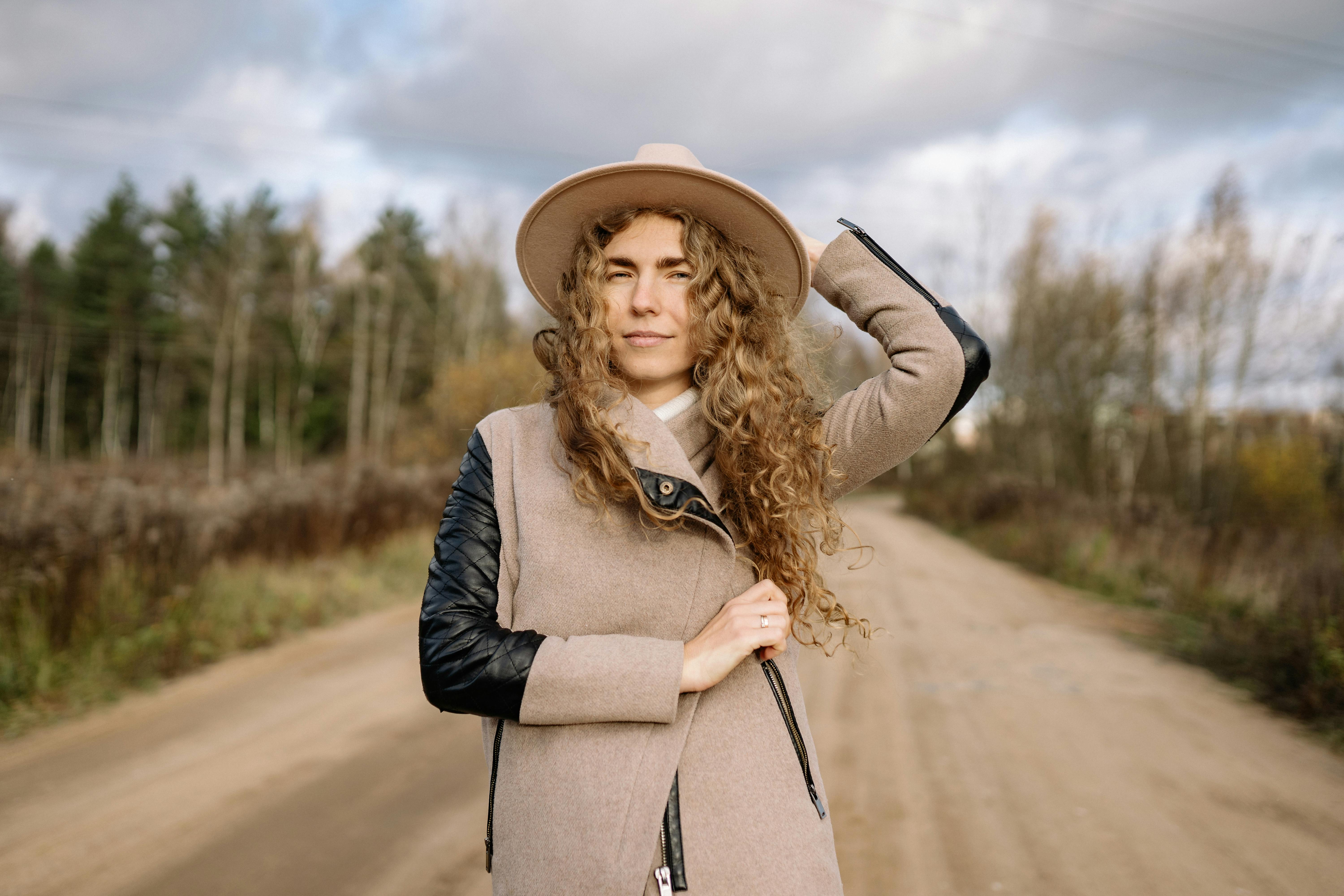 woman in hat and coat posing on road in countryside