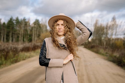 Woman in Hat and Coat Posing on Road in Countryside