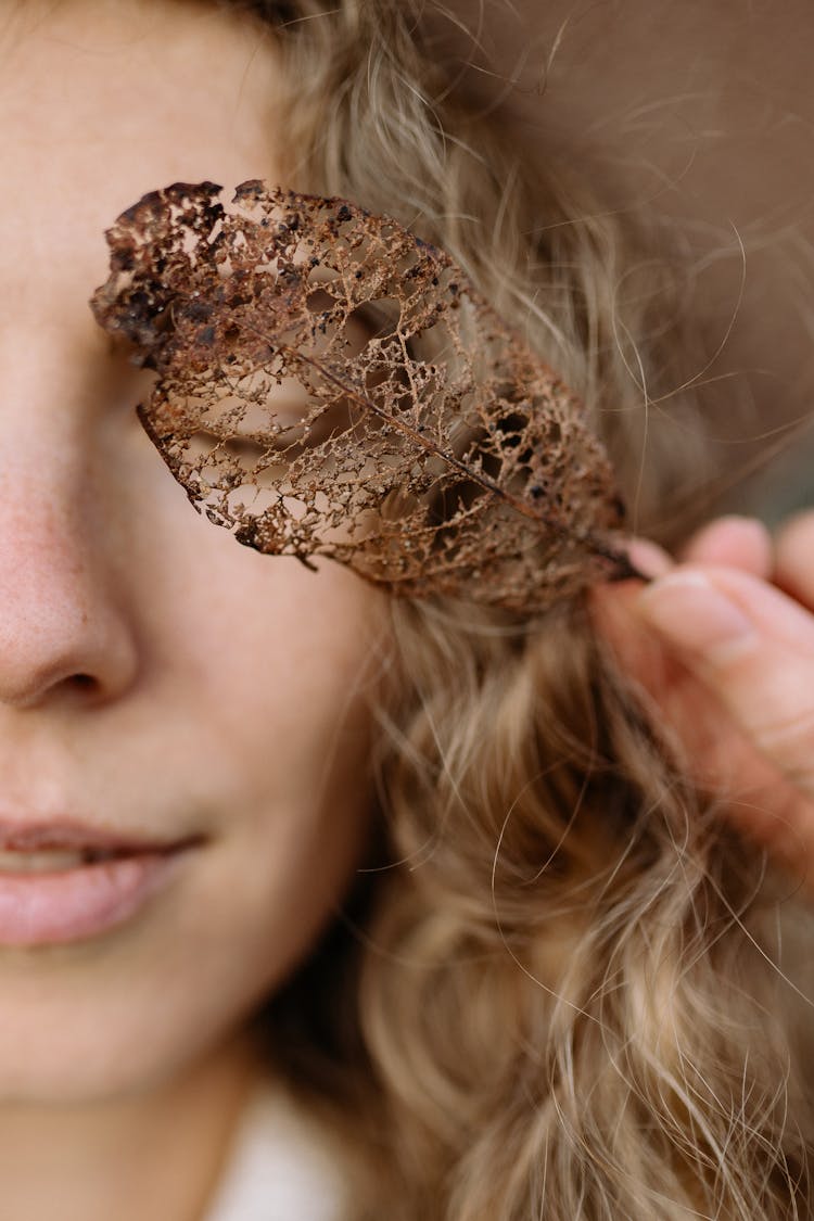 Close-up Of Woman Holding Golden Leaf On Eye Background