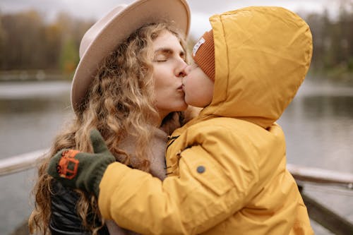 Boy in Yellow Jacket Kissing Woman Wearing Brown Hat