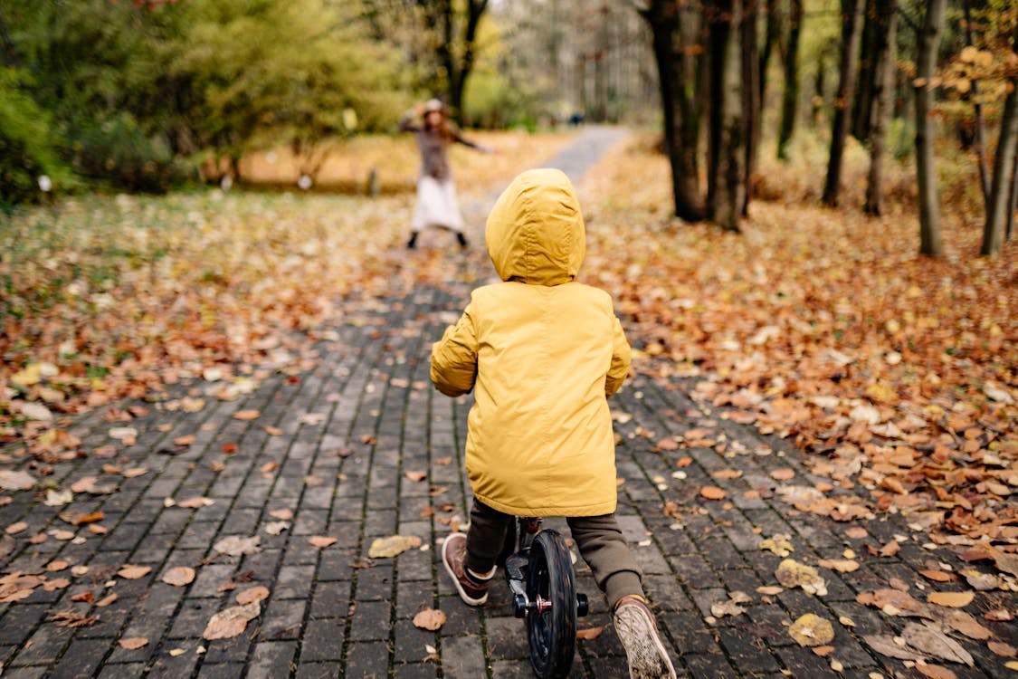 Free Child in Yellow Hoodie Jacket Riding Bicycle on Gray Concrete Pathway Stock Photo
