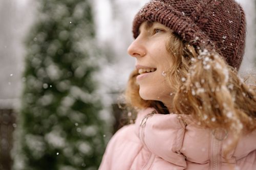 Free Close-up of a woman wearing a beanie and pink coat while enjoying a snowy winter day outside. Stock Photo
