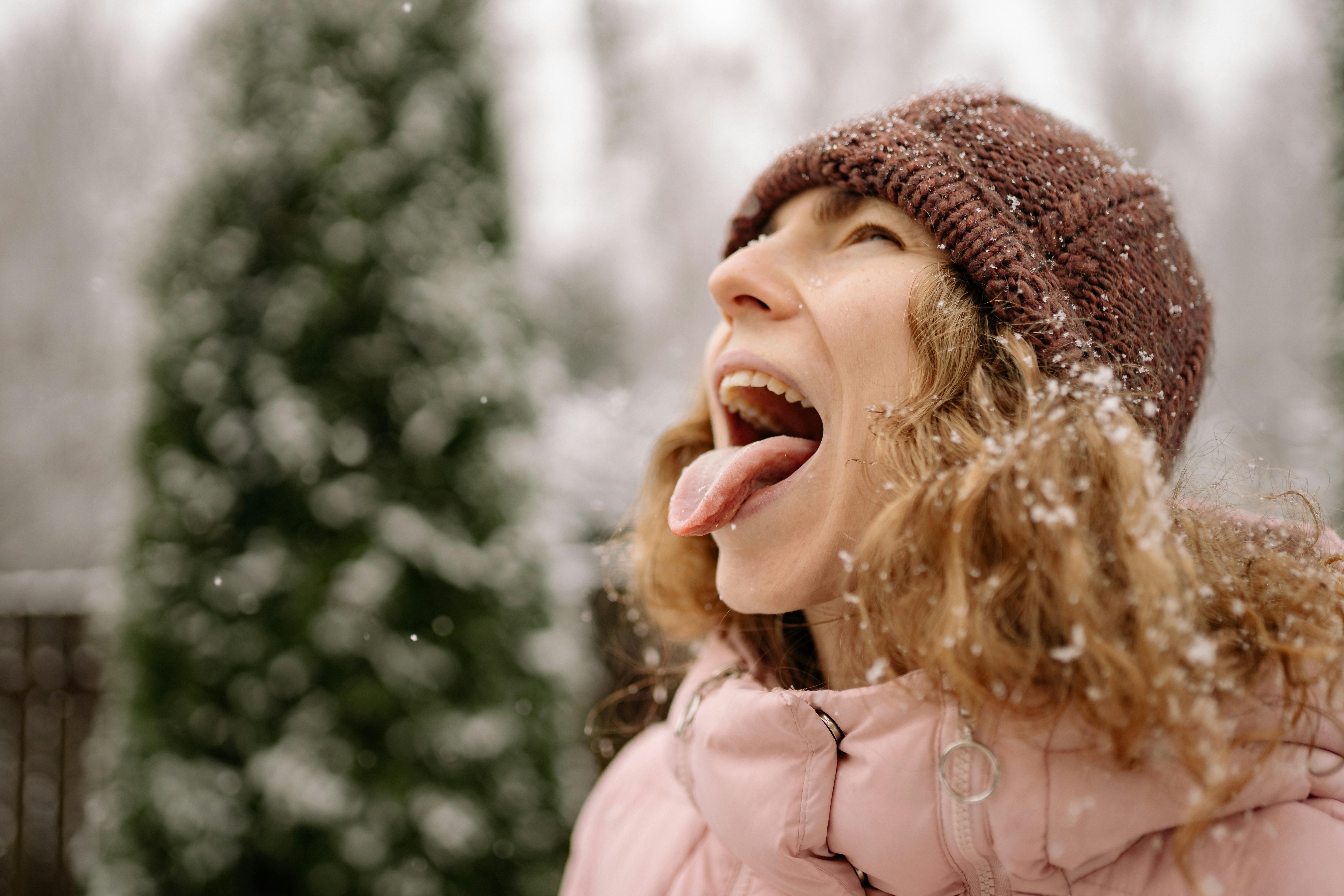 Woman enjoying the snow, catching flakes on her tongue in a playful outdoor winter scene.
