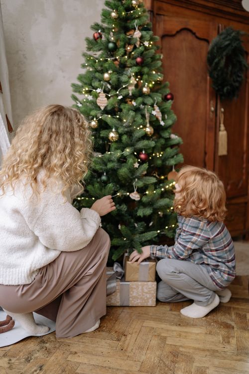 Free A parent and child decorating a Christmas tree together in a cozy indoor setting, capturing festive family moments. Stock Photo