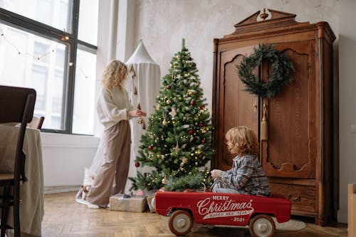 Free A mother and her son enjoy decorating a cozy indoor Christmas tree setting with festive cheer. Stock Photo