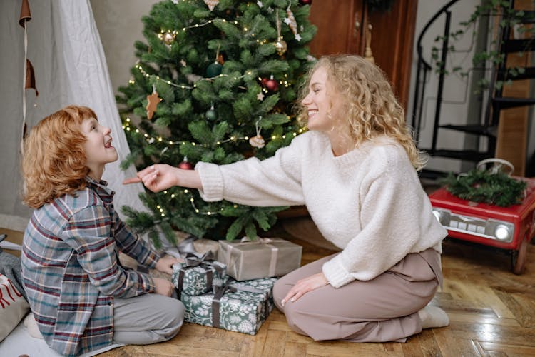 A Woman Kneeling Beside A Christmas Tree With Her Son