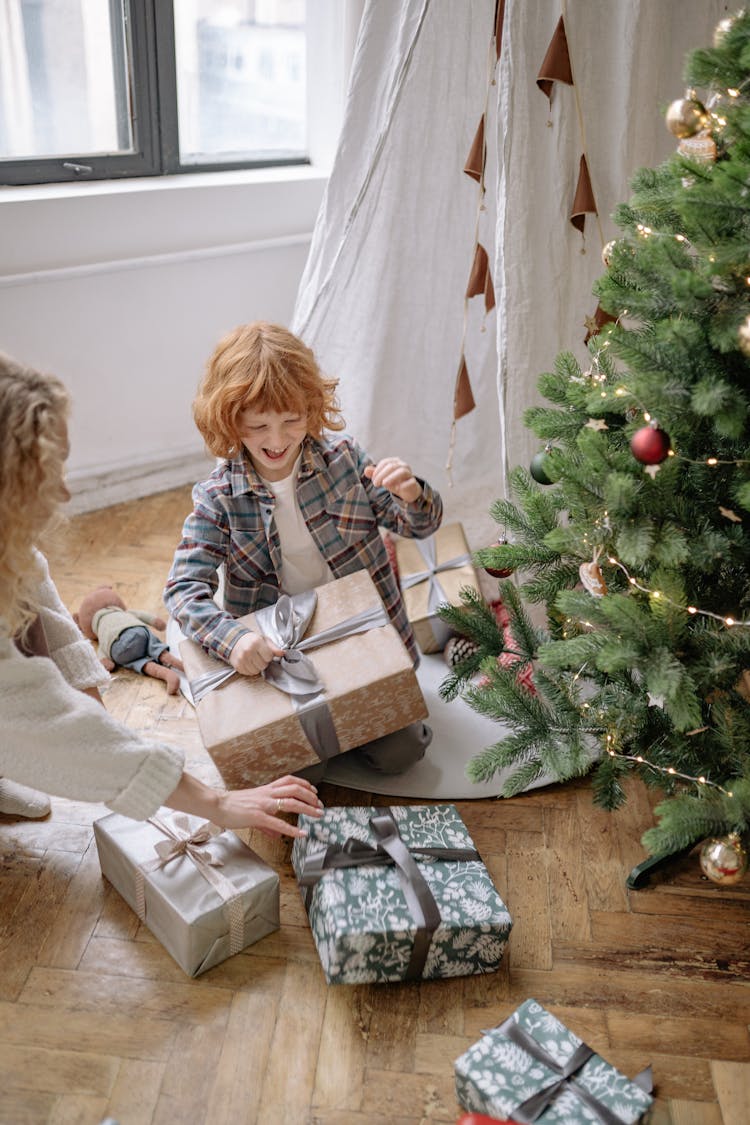 A Happy Boy Opening His Christmas Presents With His Mom