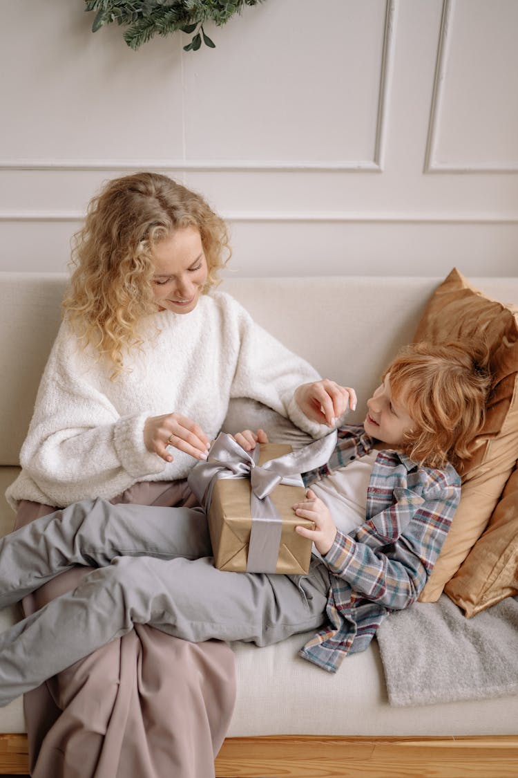 A Woman Opening A Present With Her Son On A Couch