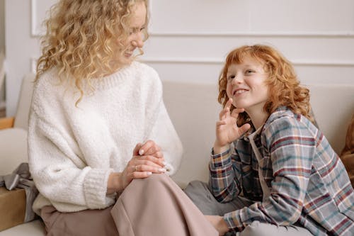 A Woman in White Top and a Boy in Plaid Shirt Smiling While Sitting