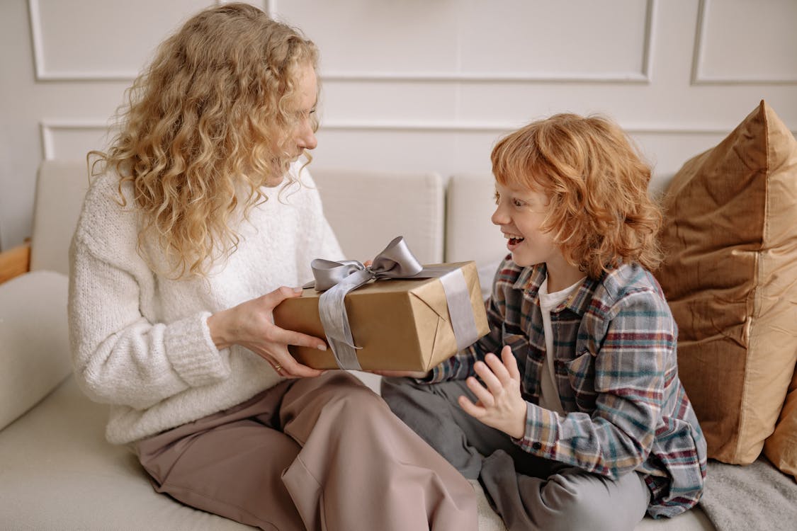 Free A Woman in White Top Handing a Gift to a Boy in Plaid Shirt Stock Photo