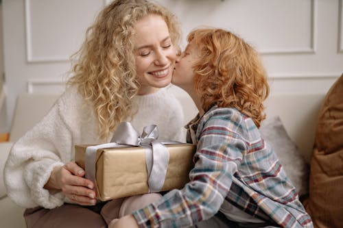 Free A Boy in Plaid Shirt Kissing a Woman in White Top Holding a Gift Box Stock Photo