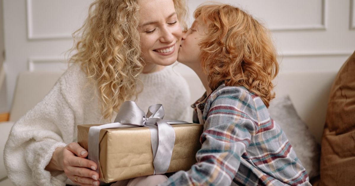 Happy mother holding a wrapped gift while her child kisses her cheek