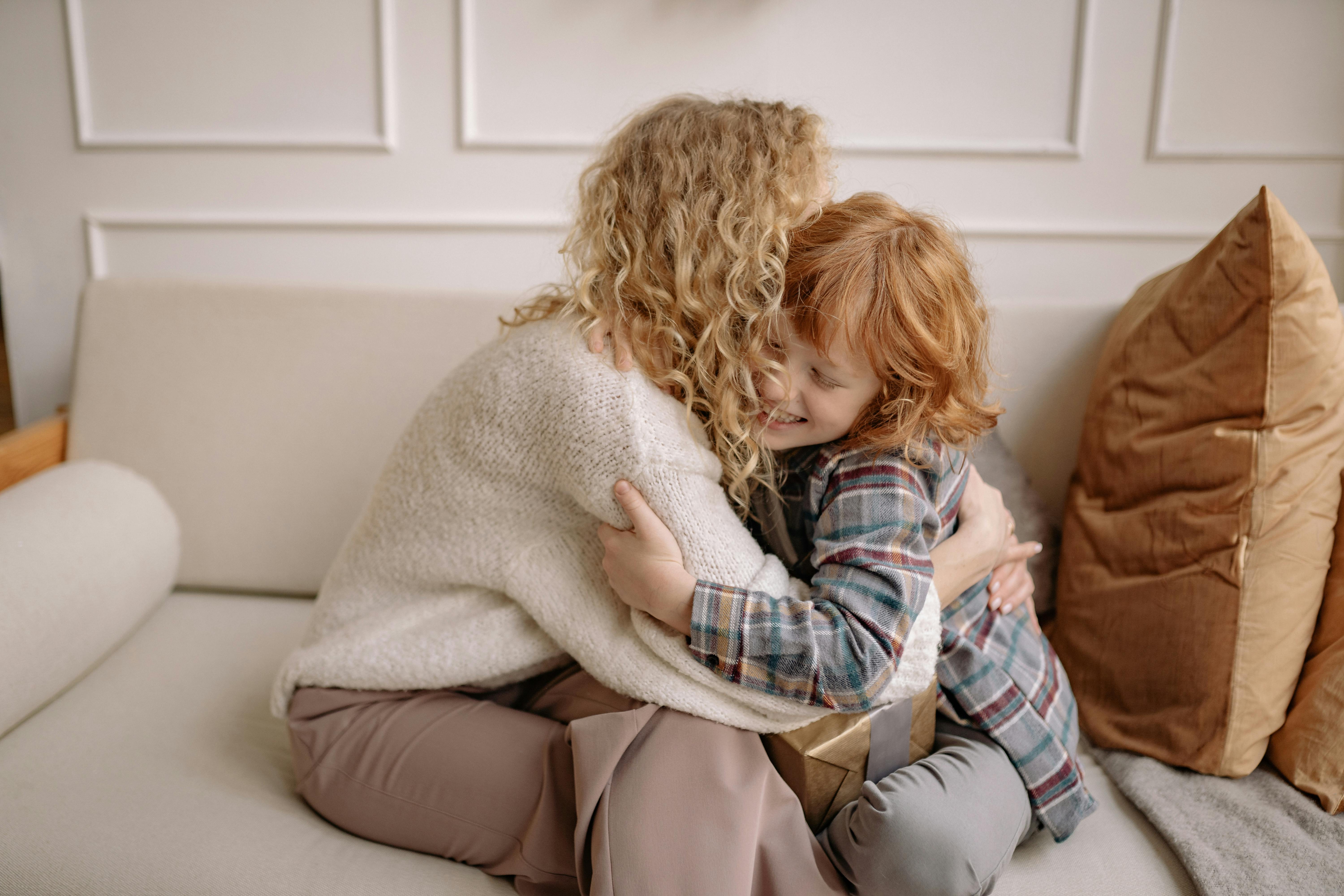 a woman and a boy with curly hair hugging each other on a couch