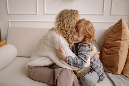 A Woman and a Boy With Curly Hair Hugging Each Other on a Couch
