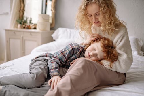 Free A mother lovingly embraces her son while seated on a bed in a cozy, softly lit room. Stock Photo