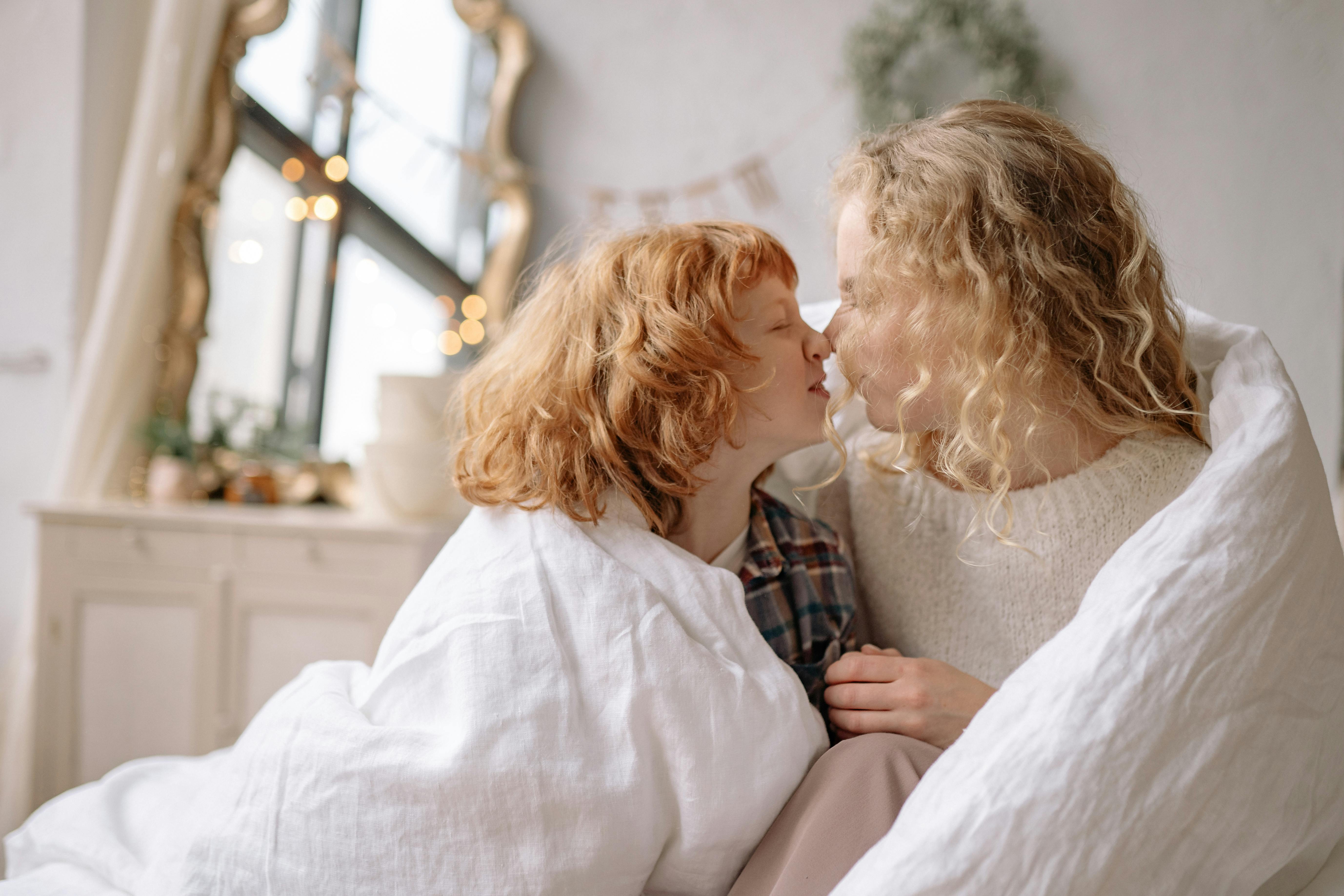 A heartwarming moment between a mother and daughter, wrapped in a cozy blanket indoors.