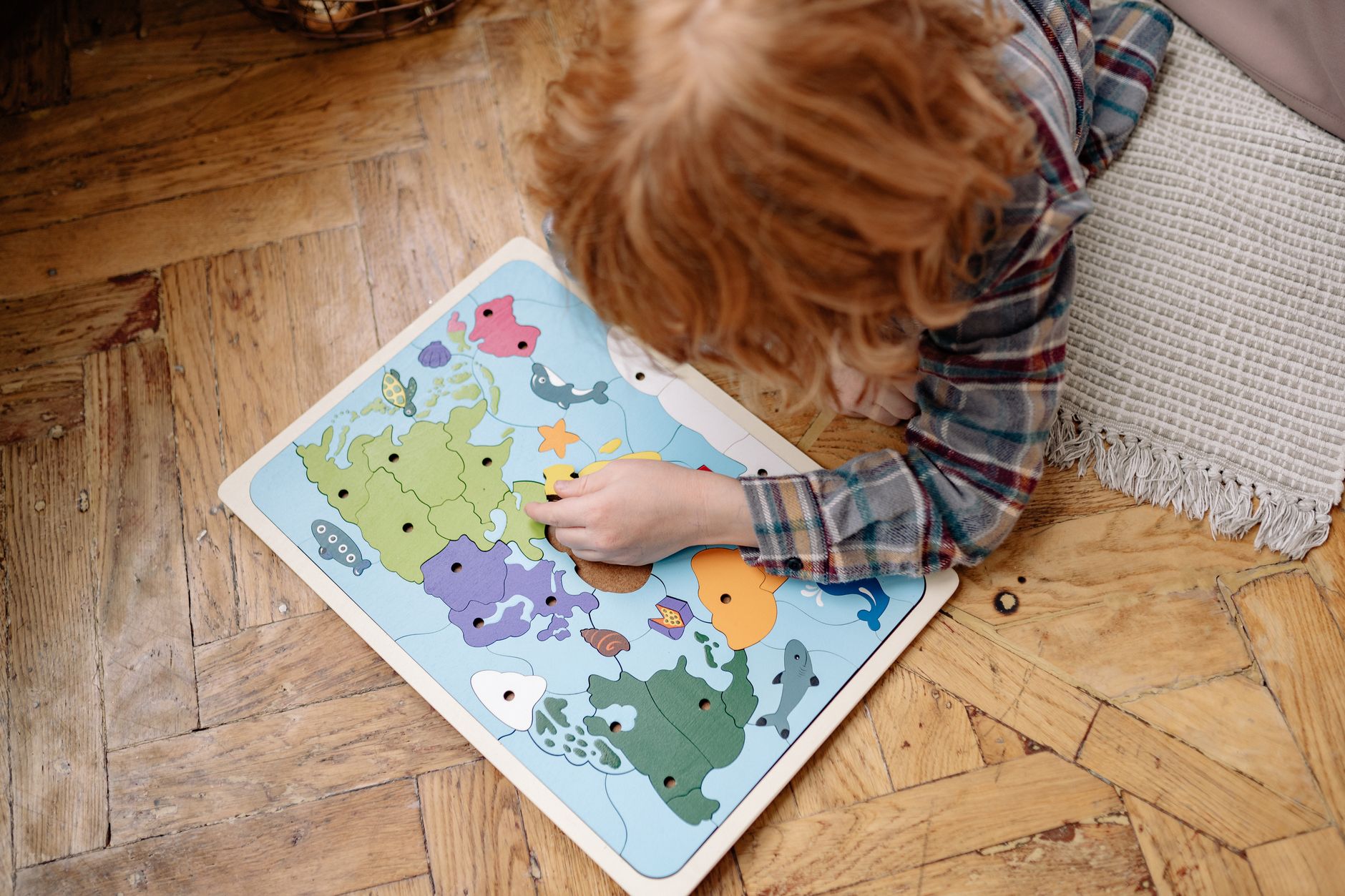 A child engaged with a colorful educational world map puzzle on a wooden floor, enhancing their problem-solving skills.